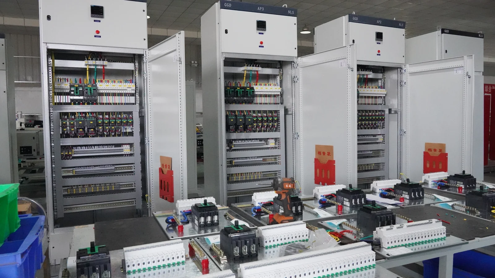 Open electrical cabinets behind workbenches holding wired electrical components